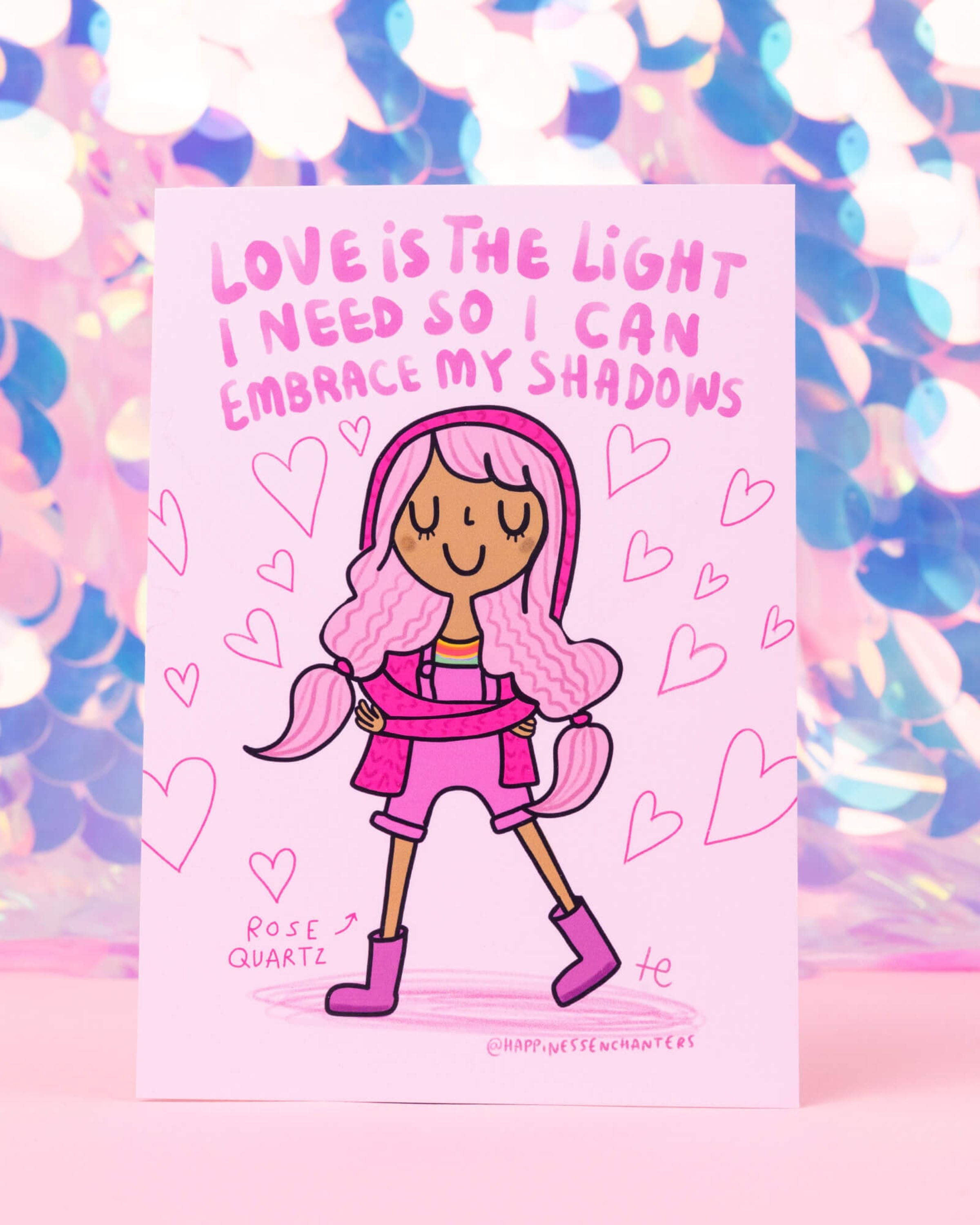 Rose Quartz postcard by Katie Abey for Happiness Enchanters, featuring a joyful girl with pink hair hugging herself surrounded by hearts. Text reads “Love is the light I need so I can embrace my shadows.” Sold by Rebel Romance, a UK small business celebrating alternative style and millennial magic.