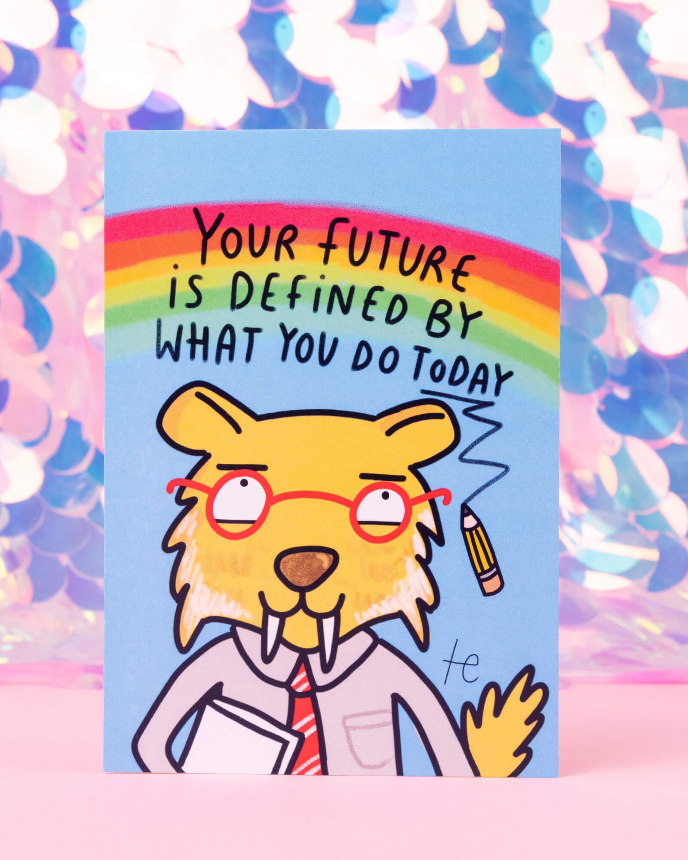 Capricorn Sabre of Success postcard illustrated by Katie Abey for Happiness Enchanters, featuring a yellow sabre-toothed character in red glasses and a tie, with a rainbow and the quote “Your future is defined by what you do today.” Sold by Rebel Romance, a UK small business celebrating alternative fashion, creativity and quirky self-expression.