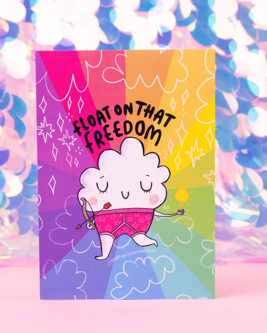 Sagittarius zodiac Floater postcard illustrated by Katie Abey for Happiness Enchanters, featuring a fluffy looking cloud character in pink shorts holding a love arrow under the phrase “Float on that freedom” with a vibrant rainbow background. Available at Rebel Romance, a UK small business celebrating magical weirdness, alternative style, and playful gifts.
