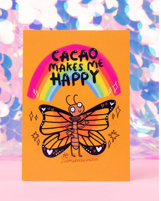 Cacao Butterfly postcard illustrated by Katie Abey for Happiness Enchanters, featuring an orange background with a whimsical butterfly, rainbow, and bold black text saying “Cacao Makes Me Happy.” Available at Rebel Romance, a UK small business selling alternative gifts and fashion.