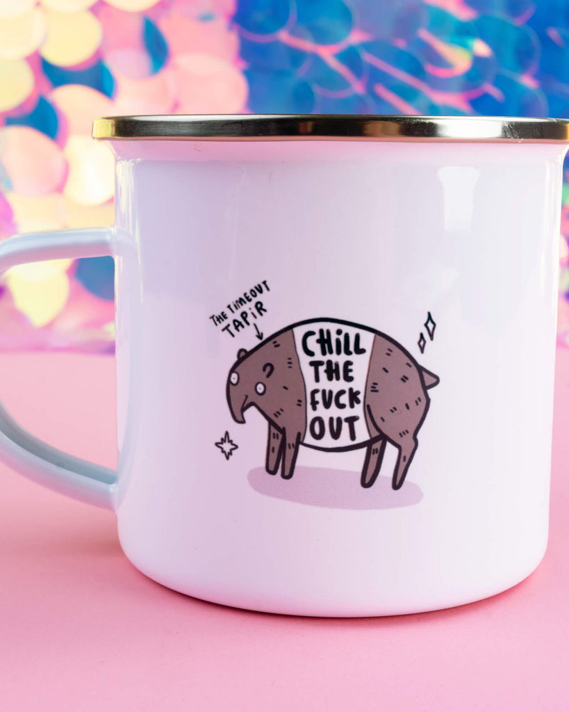 White enamel mug with a gold rim featuring the Timeout Tapir character and the phrase “Chill the F*** Out” in bold lettering. Designed by Happiness Enchanters and available at Rebel Romance, a UK small biz selling alternative homeware, fashion and gifts. Set against a pink and iridescent background.