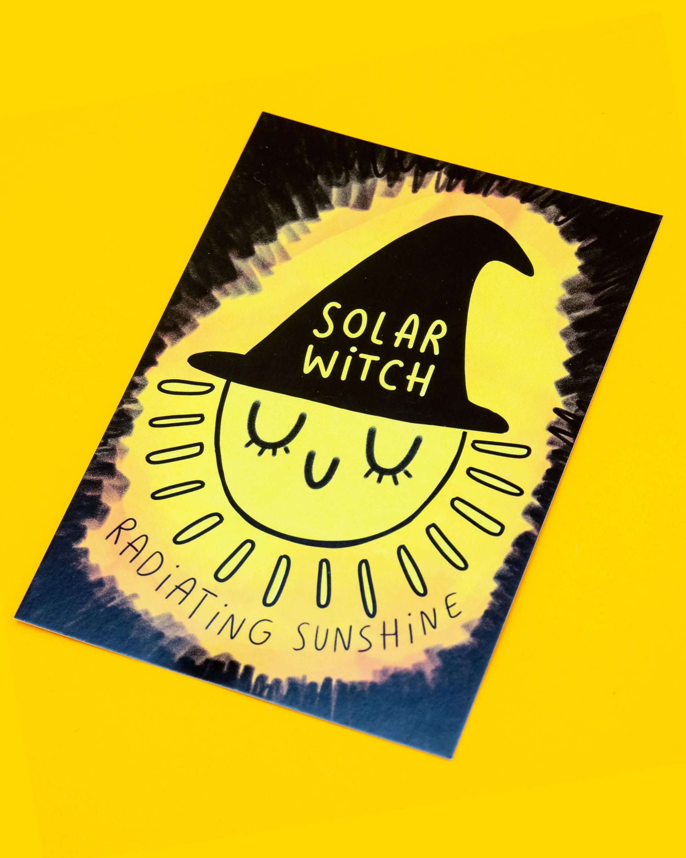A bright yellow A6 postcard from Rebel Romance featuring an illustration of a smiling sun wearing a black witch hat that reads “Solar Witch”. Around the sun are the words “Radiating Sunshine” in Katie Abey's text. This magical postcard is designed by Katie Abey and is perfect for alternative style lovers, spreading positivity and a bold, joyful vibe.