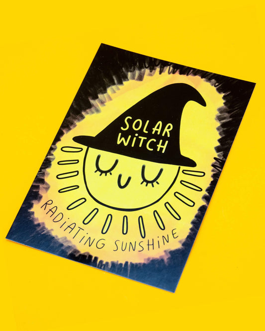 A bright yellow A6 postcard from Rebel Romance featuring an illustration of a smiling sun wearing a black witch hat that reads “Solar Witch”. Around the sun are the words “Radiating Sunshine” in Katie Abey's text. This magical postcard is designed by Katie Abey and is perfect for alternative style lovers, spreading positivity and a bold, joyful vibe.