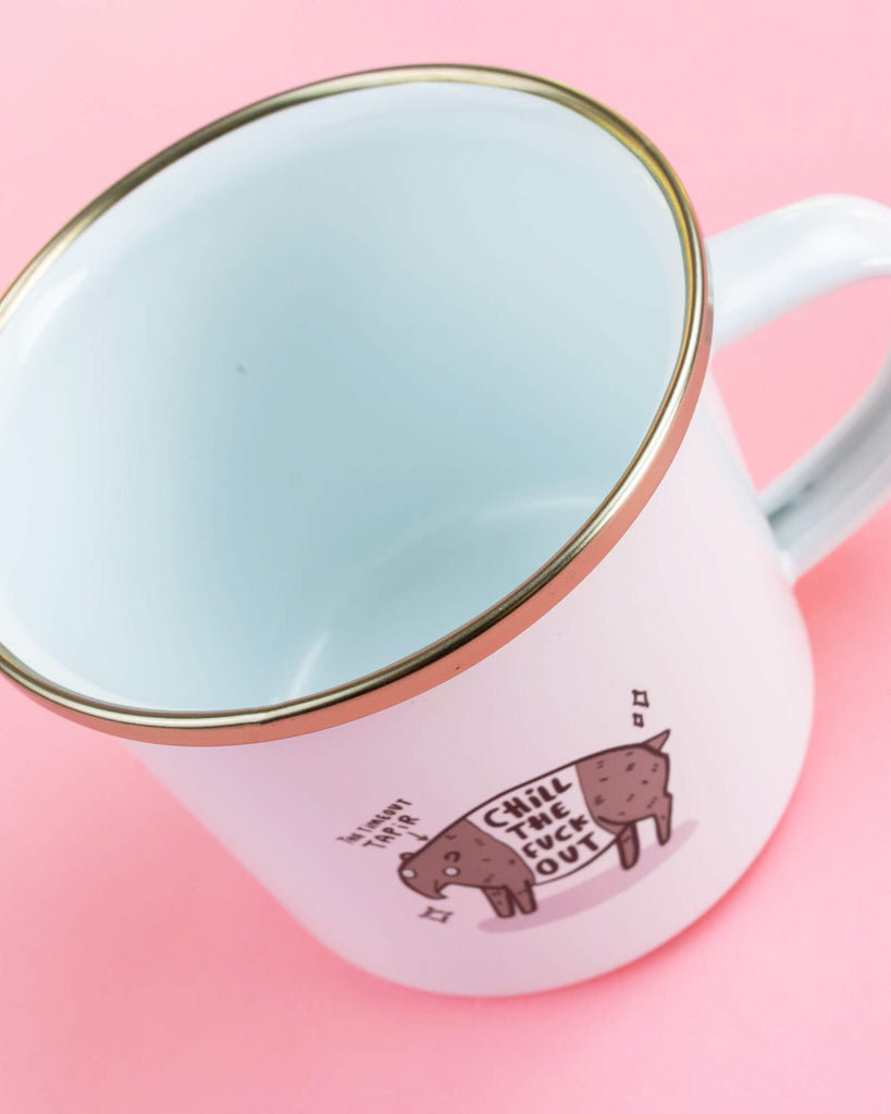 Angled view of a white enamel mug with gold rim, showing the Timeout Tapir design with the phrase “Chill the F*** Out” on a pink background. Sold by Rebel Romance, a small UK business that celebrates alternative style, homeware, fashion and gifts.