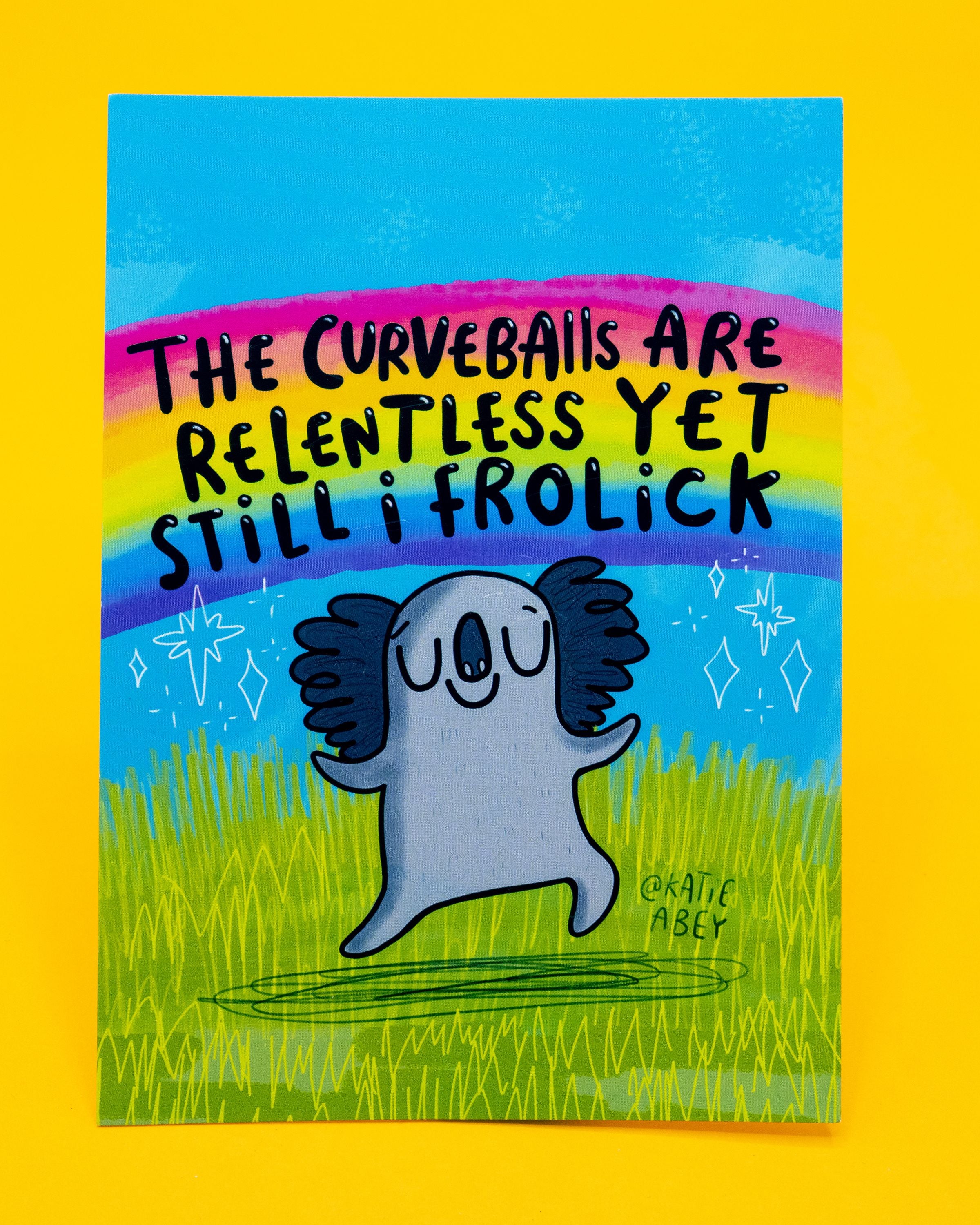 A6 postcard designed by Katie Abey and sold on Rebel Romance with a cheerful koala illustration. The koala is happily frolicking on green grass under a bright blue sky and rainbow, surrounded by sparkles. Bold black text reads: “The curveballs are relentless yet still I frolick.” A quirky, uplifting postcard perfect for millennial stationery lovers who embrace humour and positivity.
