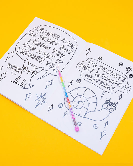 Open page of the Stay Whimsical Magical Colouring Book by Katie Abey, featuring two illustrations. Left page has “The Chihuahua of Change” with text: “Change can be scary but I know you can make it through this.” Right page shows a smiling snail with text: “No regrets only whimsical mistakes.” A rainbow pen rests across the book.
