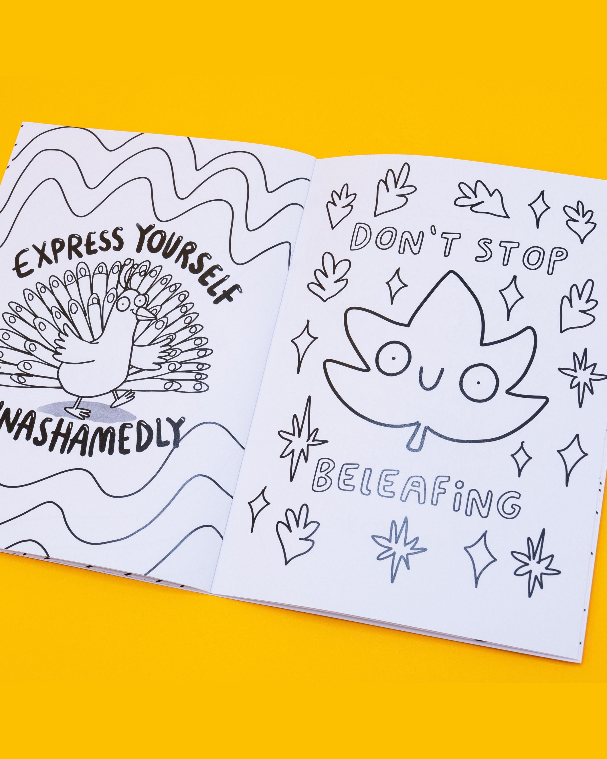 Open page of the Stay Whimsical Magical Colouring Book by Katie Abey, showing black-and-white line art. Left page has a peacock with the text: “Express yourself unashamedly.” Right page shows a smiling leaf with text: “Don’t stop beleafing,” surrounded by stars and small leaves. Sold by a Rebel Romance, a small UK business celebrating individuality through fashion, stationery and gifts. Designed by UK illustrator 