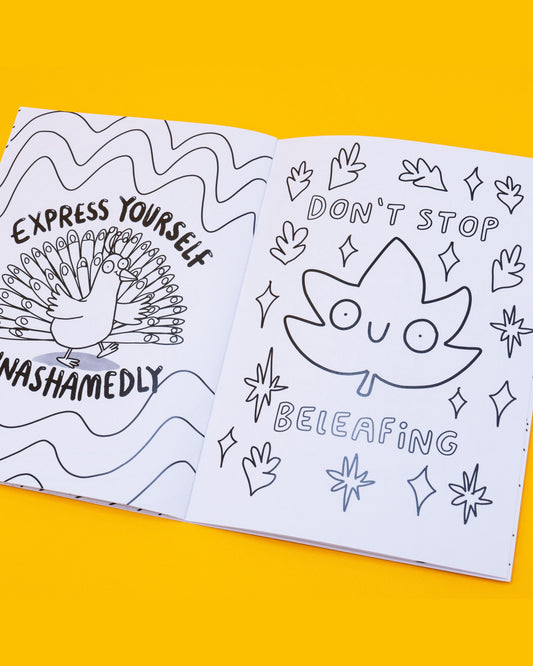 Open page of the Stay Whimsical Magical Colouring Book by Katie Abey, showing black-and-white line art. Left page has a peacock with the text: “Express yourself unashamedly.” Right page shows a smiling leaf with text: “Don’t stop beleafing,” surrounded by stars and small leaves. Sold by a Rebel Romance, a small UK business celebrating individuality through fashion, stationery and gifts. Designed by UK illustrator 