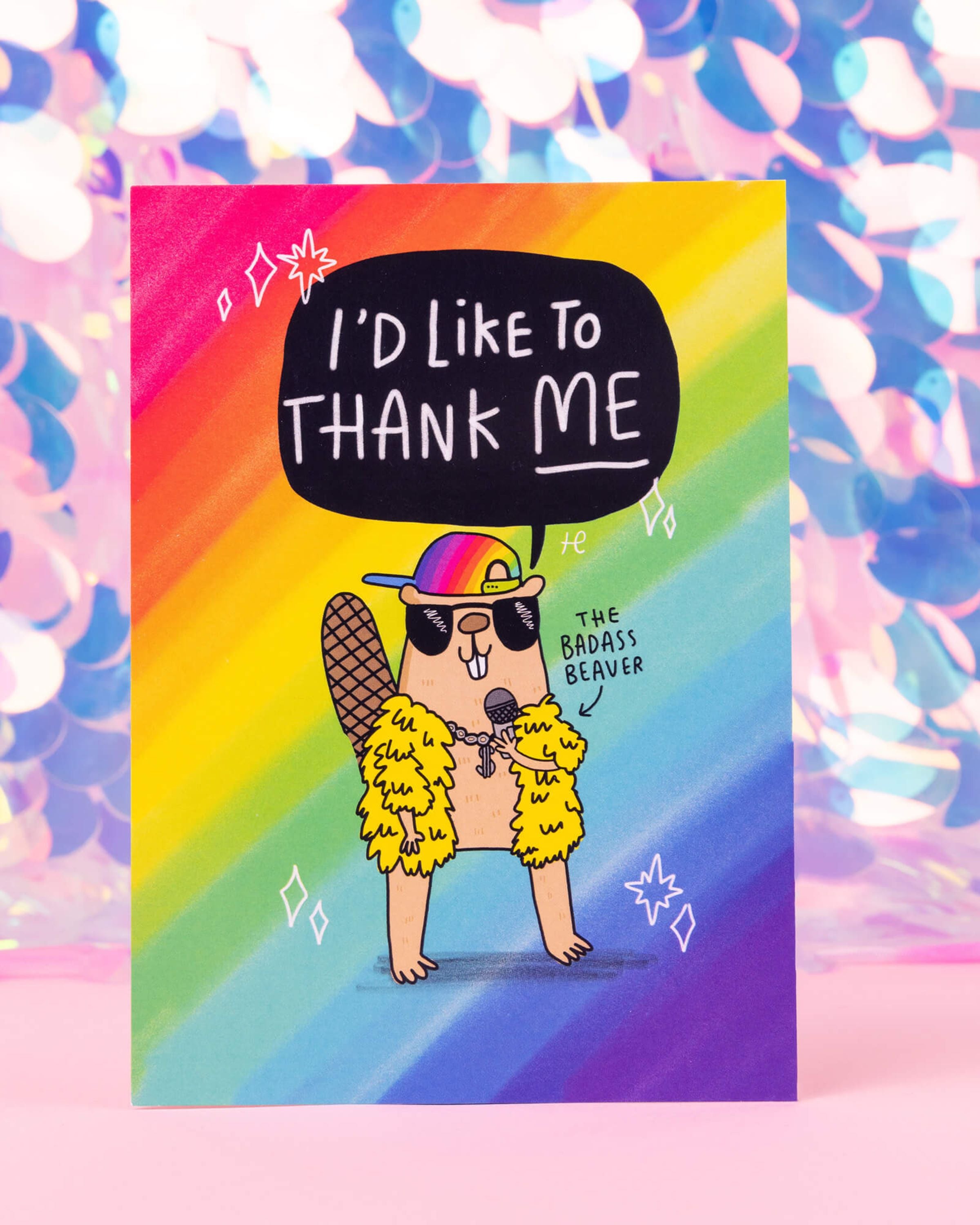 A bold rainbow postcard available at Rebel Romance featuring a beaver in sunglasses, gold chains, and a rainbow cap, saying “I’d like to thank me.” Labelled as “The Badass Beaver,” this design is Illustrated by Katie Abey for Happiness Enchanters.