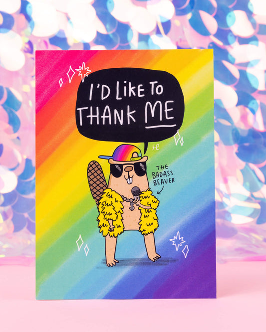 A bold rainbow postcard available at Rebel Romance featuring a beaver in sunglasses, gold chains, and a rainbow cap, saying “I’d like to thank me.” Labelled as “The Badass Beaver,” this design is Illustrated by Katie Abey for Happiness Enchanters.