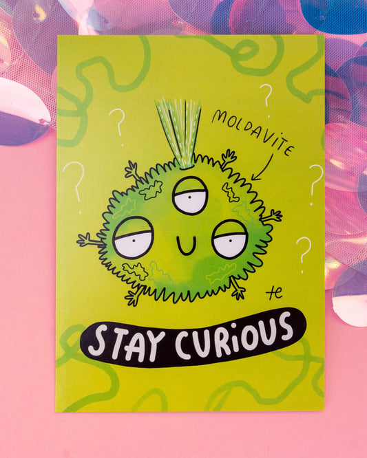 Bright green A6 postcard from Rebel Romance featuring a cartoon Moldavite crystal character with three eyes, wild tufts of hair, and surrounded by question marks. The postcard reads “Stay Curious” in bold letters. Illustrated by Katie Abey for the Happiness Enchanters collection, perfect for crystal lovers and cosmic explorers. Styled on a pink background with shiny iridescent textures.