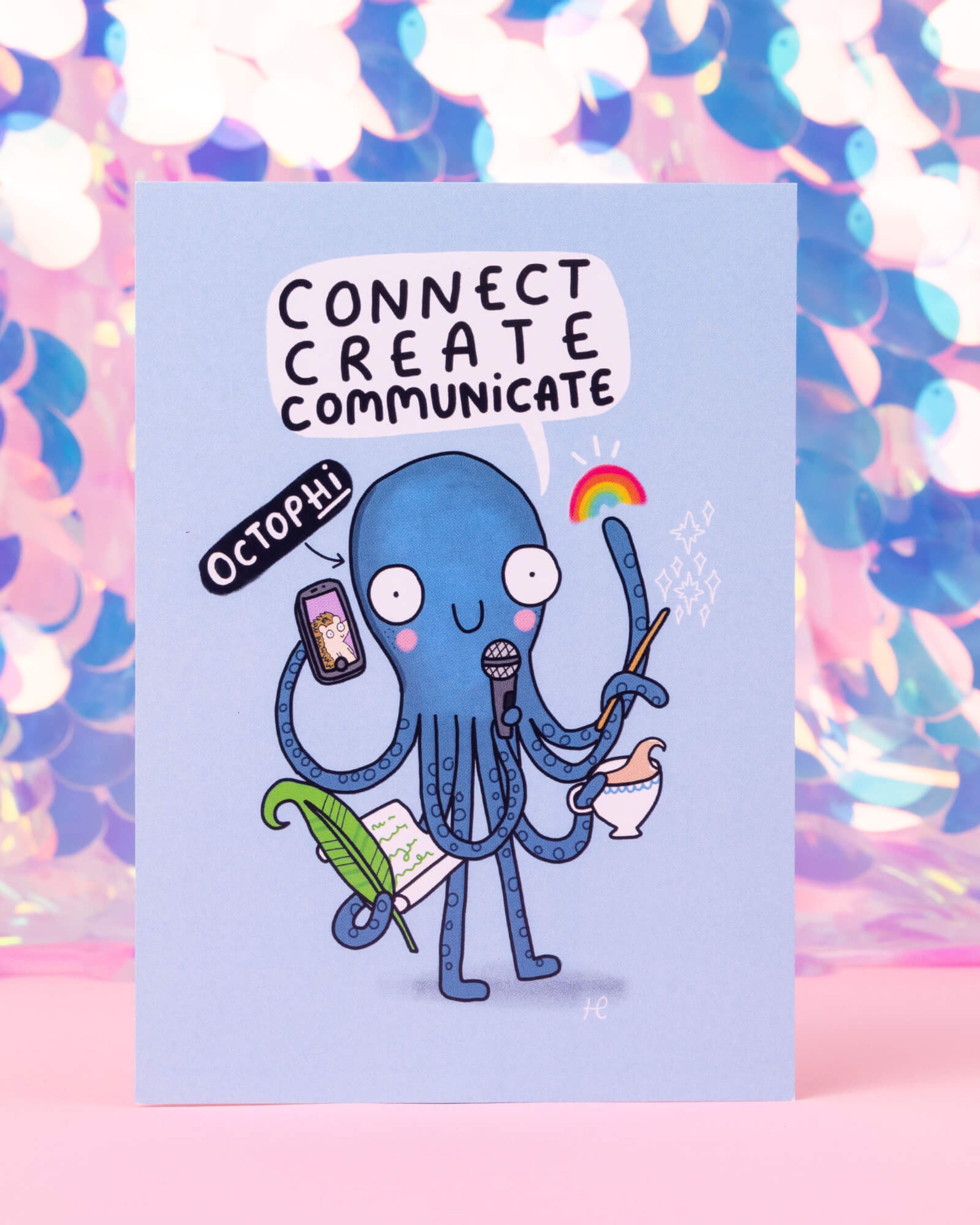 A colourful Gemini themed postcard designed by Happiness Enchanters, available at Rebel Romance. It features a Katie Abey illustrated blue octopus named Octophi with eight arms multitasking, holding a mic, phone, quill, scroll, paintbrush, and tea cup. The speech bubble reads “Connect, Create, Communicate” against a pastel blue background. Perfect for lovers of astrology, creativity, and cute character art.