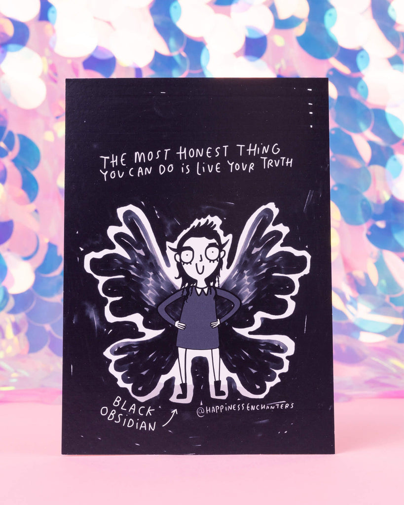 A black and white postcard from Rebel Romance featuring a bold character with black wings and pointed winged eyeliner, standing confidently with hands on hips. Surrounded by stars, it reads: “The most honest thing you can do is live your truth.” Illustrated by Katie Abey for Happiness Enchanters.