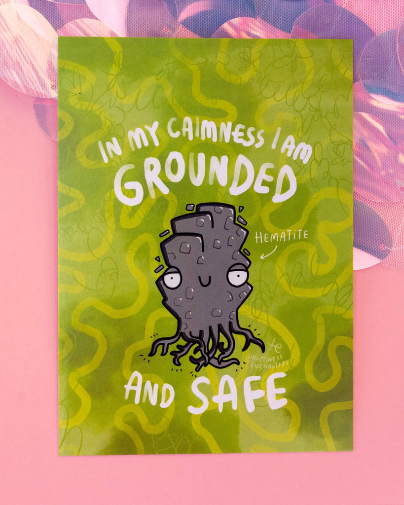 Green postcard featuring a cartoon-style Hematite crystal character with roots illustrated by Katie Abey and the affirmation “In my calmness I am grounded and safe.” Product by Happiness Enchanters and available at Rebel Romance, a UK small business selling alternative stationery, fashion, and gifts.