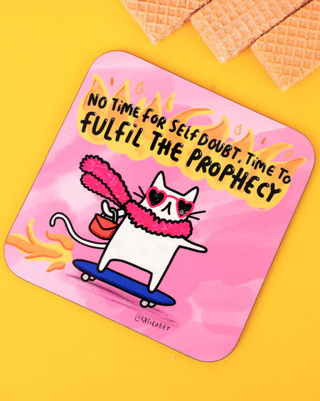 Flat-lay image of a Katie Abey illustrated coaster with a flaming pink design. The coaster features a fierce cat in heart sunglasses and a feather boa skating with purpose. The text above reads “No time for self doubt, time to fulfil the prophecy” in a fiery bold font. Wafers are placed above the coaster on a yellow surface.