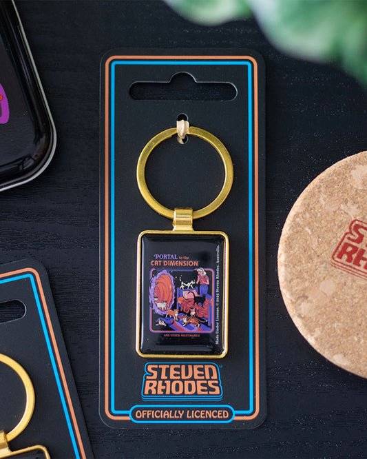 Steven Rhodes ‘Portal to the Cat Dimension’ keyring on Rebel Romance backing card. The gold-framed enamel accessory shows cats bursting through a glowing portal in a retro scene. Alternative gift for cat lovers, collectors, and anyone who enjoys quirky gothic humour.