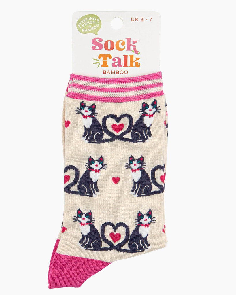 A pair of cream bamboo socks with a playful cat design, featuring black and white cats with their tails forming heart shapes, scattered pink hearts, and a striped pink cuff.