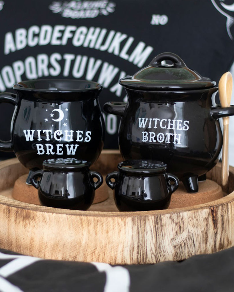 A set of ceramic cauldron-shaped salt and pepper shakers in glossy black, styled alongside matching kitchenware with "Witches Brew" and "Witches Broth" text. Each shaker has two handles and three legs, adding a spooky yet stylish touch. Perfect for gothic and alternative home decor lovers. Sold by Rebel Romance, a UK small business celebrating extraordinary aesthetics.
