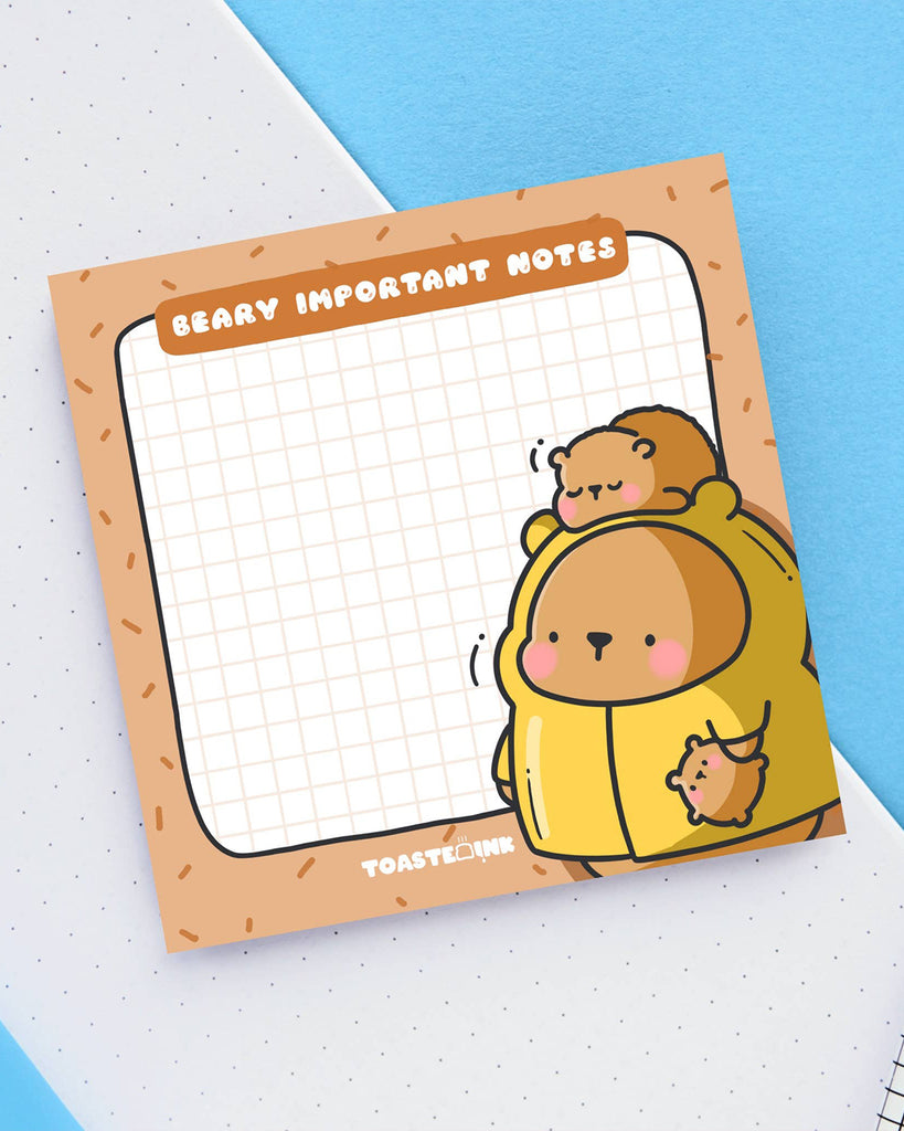 Cute bear sticky notes designed by Toastedink and available at Rebel Romance. Features grid paper and the phrase "Beary Important Notes" with a sleepy bear illustration. Displayed on a blue and white paper background.