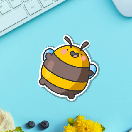 Glossy vinyl sticker of a round, cartoon-style yellow and brown bumblebee jumping happily with pink cheeks and arms raised. Displayed on a blue background. Fun and cute waterproof sticker, perfect for decorating laptops and notebooks.