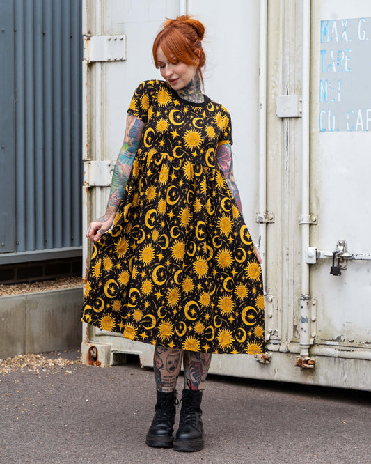 Front view of Erin in the Rebel Romance Celestial Midi Dress, a black stretch cotton smock-style midi featuring a yellow sun and moon print. The relaxed shape, short sleeves, and pockets make this alternative fashion piece both stylish and comfortable.