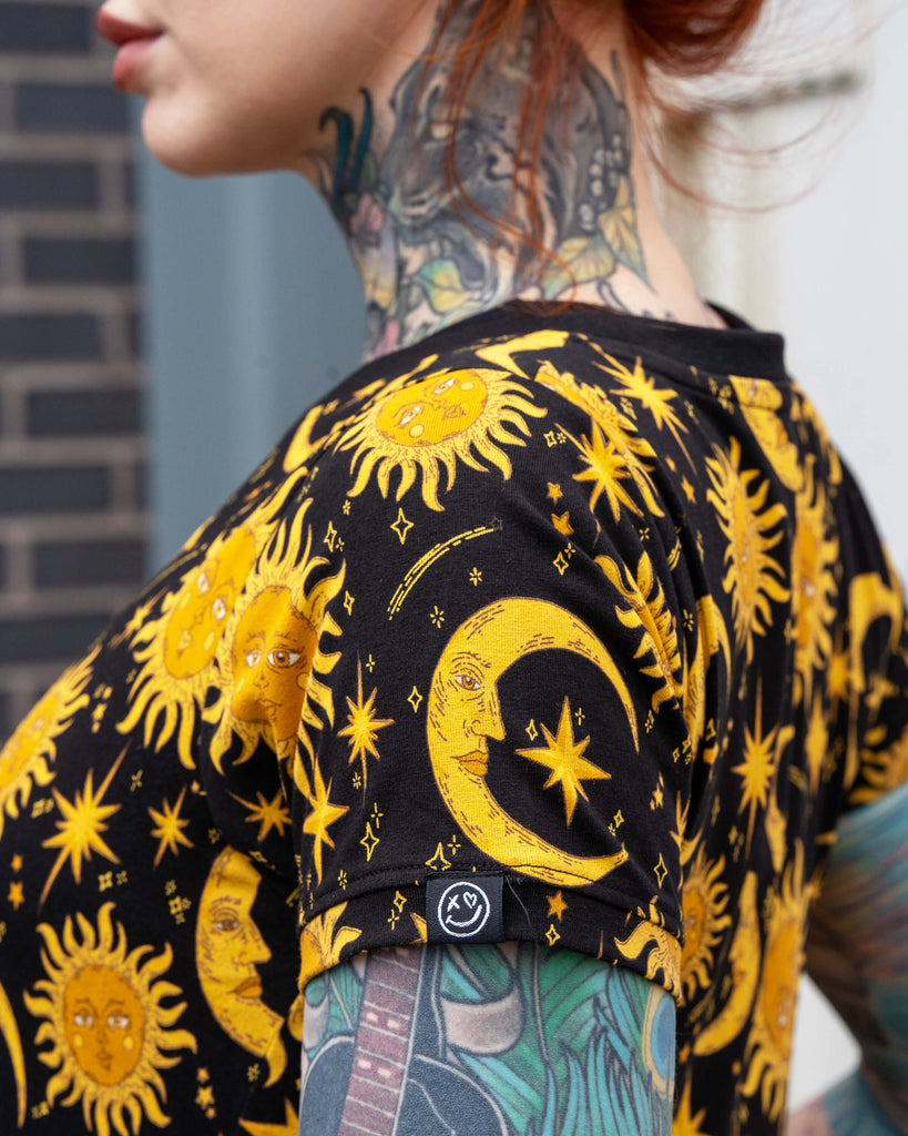 Side close-up of Erin modelling the Rebel Romance Celestial Midi Dress. The yellow celestial print with moons, suns, and stars stands out on black stretch cotton fabric. A comfy and stylish midi dress for alternative and witchy wardrobes.