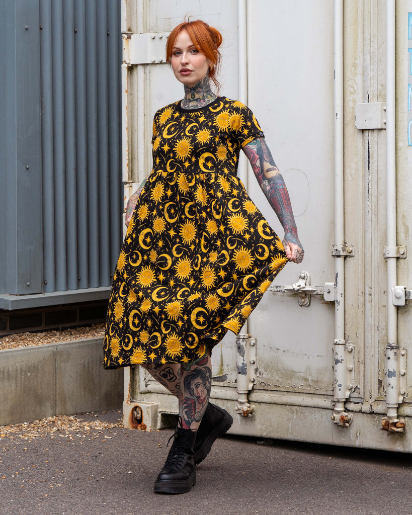 Erin posing in the Rebel Romance Celestial Midi Dress, made in stretch cotton with a bold yellow celestial sun and moon print on black. The relaxed smock style and midi length create a flattering, alternative fashion silhouette.