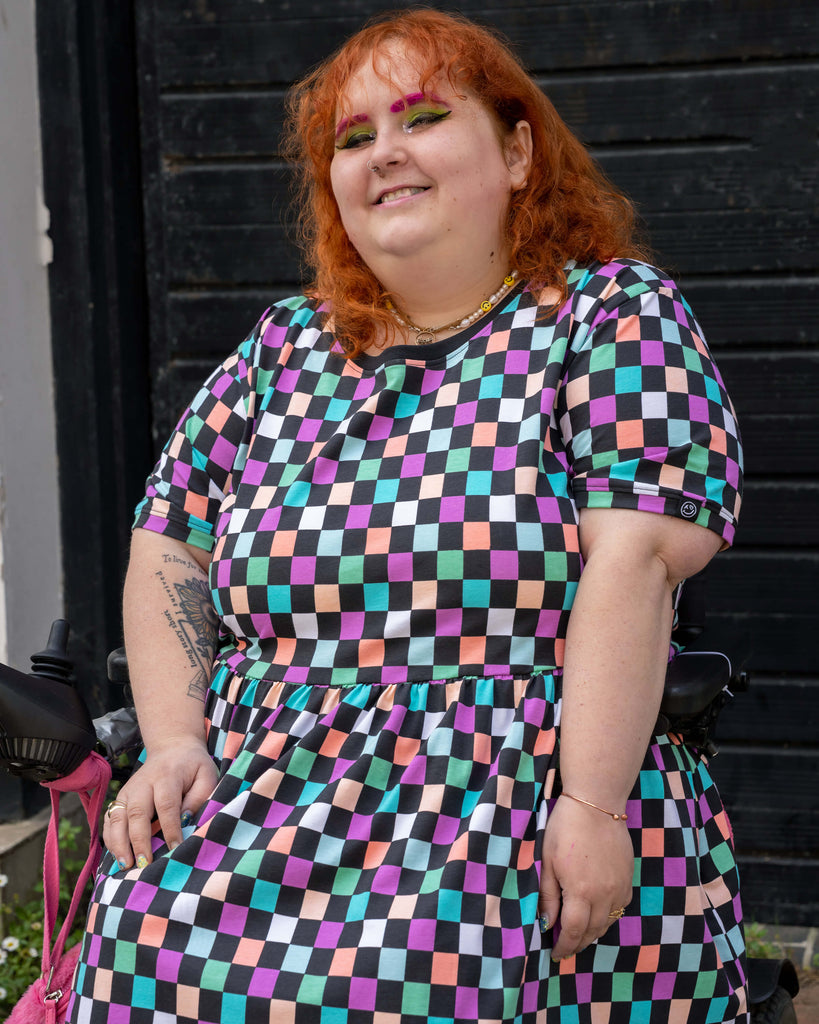 Close-up of Lauren wearing the Rebel Romance Checkerboard Stretch Smock Dress, showcasing the soft stretchy fabric and colourful check print. Designed for comfort, joy, and expressive alternative fashion in all sizes.