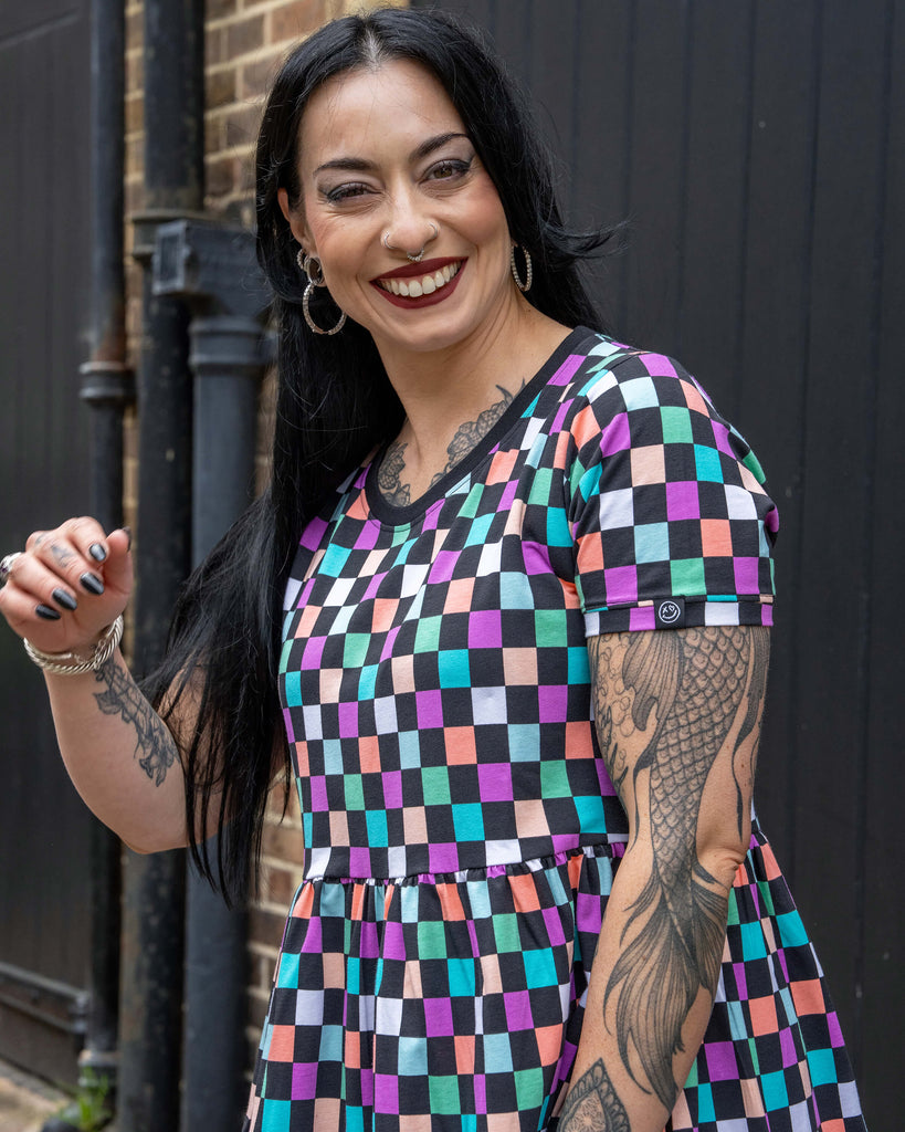 Close-up of Carmen in the Rebel Romance Checkerboard Stretch Smock Dress, showing the bold pastel check print and sleeve detail with Rebel Romance smiley tag. A statement dress full of colour and character.