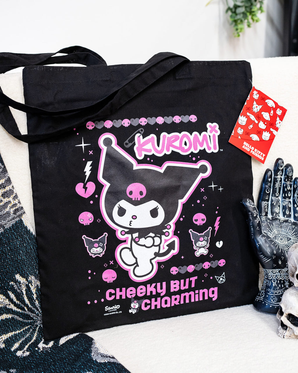 A bold black tote bag featuring Kuromi, the cheeky yet charming Sanrio character, in her signature mischievous pose surrounded by pink skulls and hearts. Designed with playful text and vibrant details, this tote is part of Rebel Romance’s unique collection of alternative and retro-branded merchandise. Perfect for fans of kawaii and gothic aesthetics, blending cuteness with edge.
