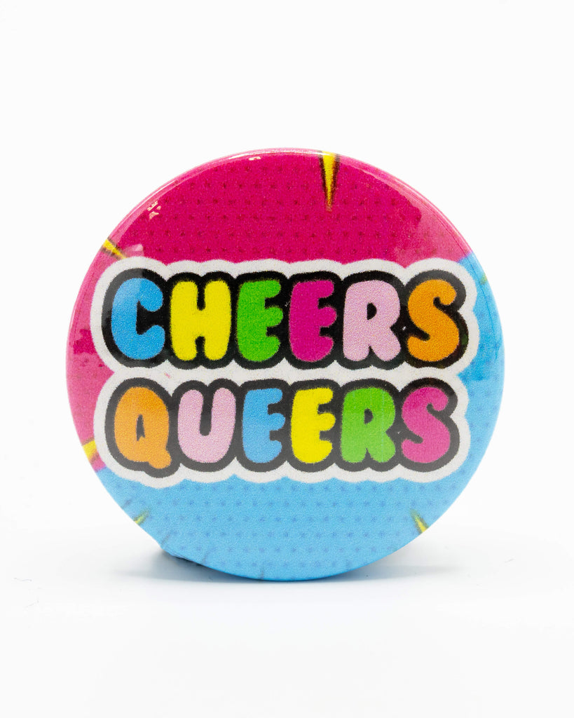 Rebel Romance "Cheers Queers" button pin badge on a white background, featuring rainbow bubble text over a bold comic-style pink and blue backdrop. Designed by Bite Your Granny, this colourful LGBTQ+ accessory adds a playful and proud statement to any outfit or bag. Part of Rebel Romance’s alternative gift range celebrating queer identity, uniqueness, and bold self-expression.
