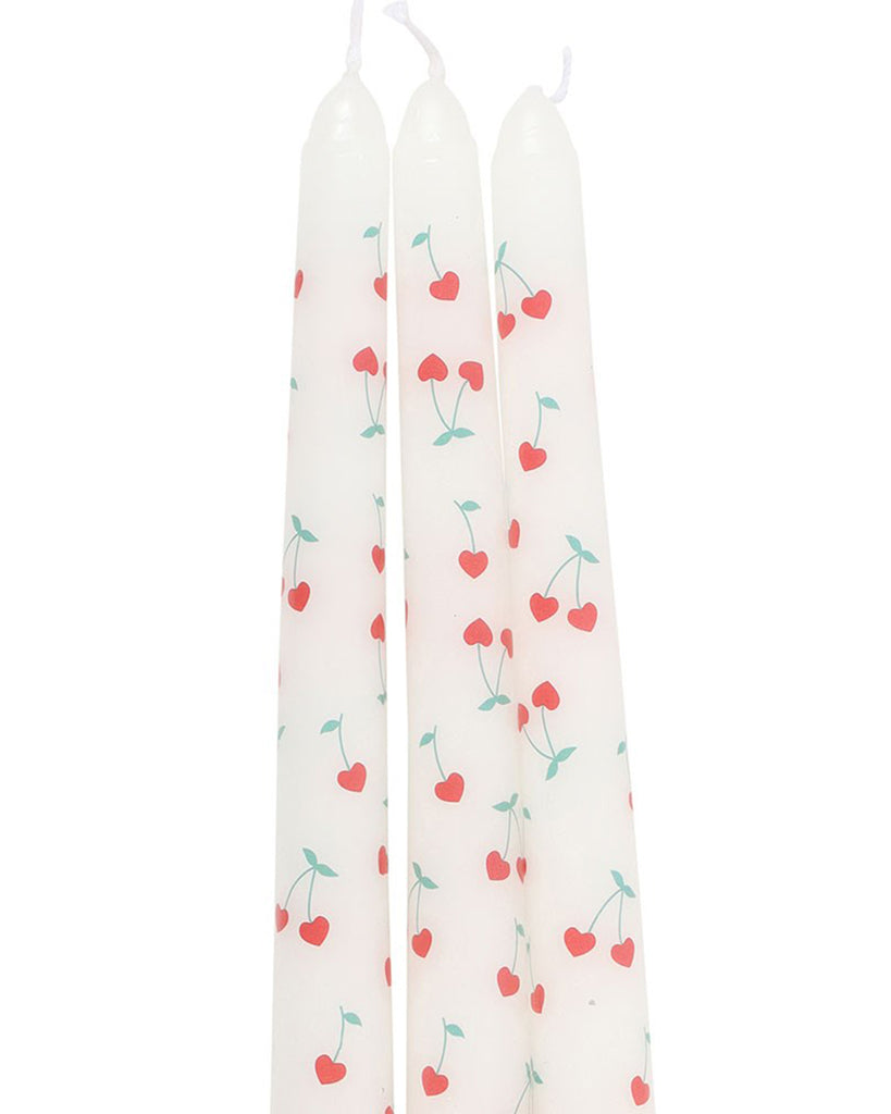 Close-up of the three Heart Cherry Taper Candles outside their packaging. Each white candle is decorated with heart-shaped cherry designs, featuring bright red cherries with green stems, creating a playful and romantic aesthetic.