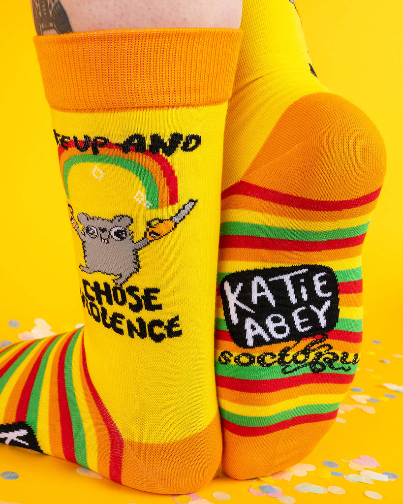 Side view of the hamster socks, showing the full design of a chainsaw-wielding hamster beneath a rainbow. The rainbow-striped soles feature the Katie Abey x Soctopus branding. Quirky and colourful with attitude.