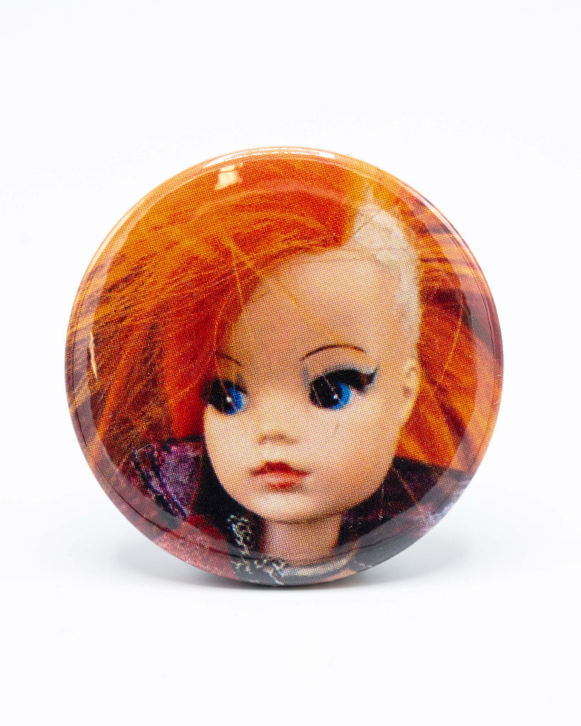 Button badge with a doll's face featuring red hair and blue eyes, a retro punk sindy design from Bite Your Granny.