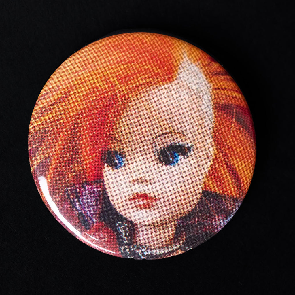 A 38mm high-gloss pin badge featuring a retro Sindy doll with bright orange punk hair and bold makeup. Designed by Bite Your Granny, celebrating offbeat nostalgia and edgy style.