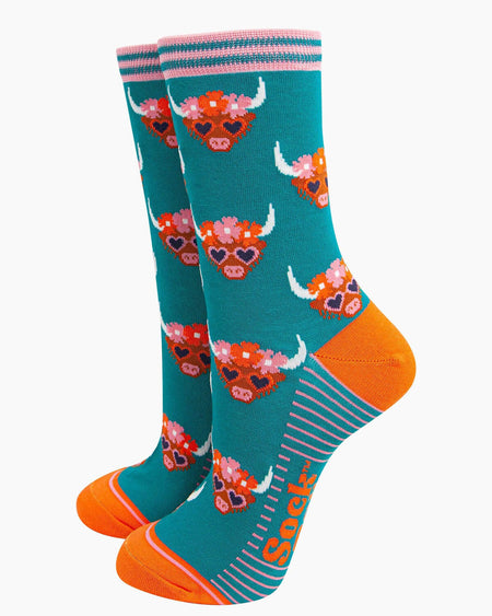 (Socks Standing Up): A pair of bamboo Highland cow socks displayed upright, highlighting the fun farmyard design, bright teal fabric, and bold orange details.