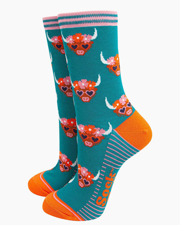 (Socks Standing Up): A pair of bamboo Highland cow socks displayed upright, highlighting the fun farmyard design, bright teal fabric, and bold orange details.