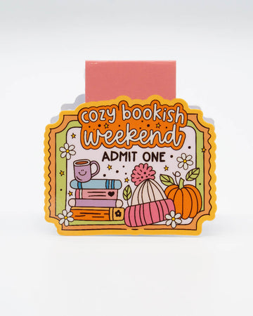 Front view of the Cozy Bookish Weekend Magnetic Bookmark from Rebel Romance, shaped like a colourful ticket with illustrations of books, a smiling mug, a pumpkin, and flowers. Features the words “Cozy Bookish Weekend – Admit One.” Ideal for readers, autumn lovers, and fans of adorable, alternative stationery. A fun and functional gift for millennials who love to get snug with a good book.