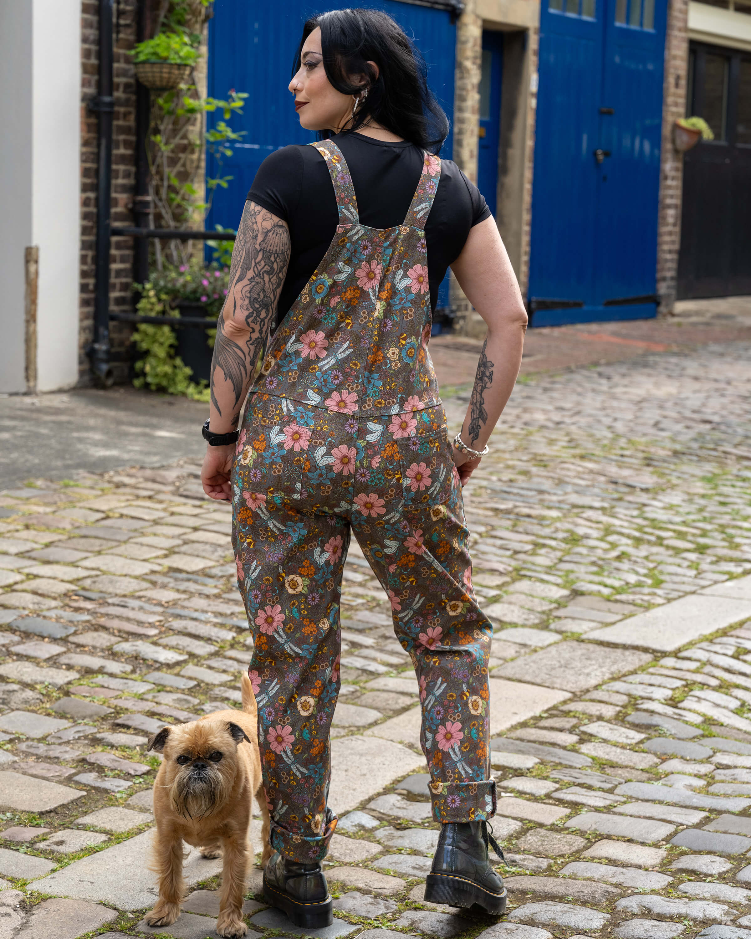 Back view of Carmen wearing Rebel Romance CottageCore Twill Dungarees, showing adjustable straps and all-over floral and insect pattern with bees, dragonflies, and flowers.