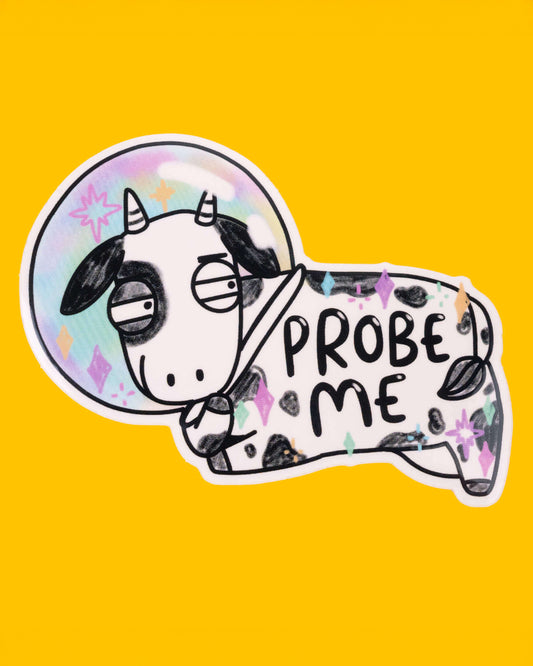 A silly sticker of a black and white cow in a rainbow-coloured space helmet, with the text "PROBE ME" on its body. The cow has a bored expression, and the background is bright yellow. This quirky design is from Katie Abey, and stocked by Rebel Romance. 
