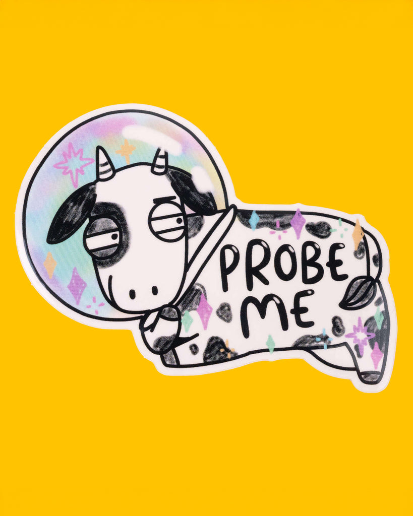 A silly sticker of a black and white cow in a rainbow-coloured space helmet, with the text "PROBE ME" on its body. The cow has a bored expression, and the background is bright yellow. This quirky design is from Katie Abey, and stocked by Rebel Romance. 