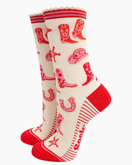 A pair of cream bamboo socks with a western cowgirl print, featuring cowboy boots, sheriff stars, cowboy hats, and horseshoes in red and pink.