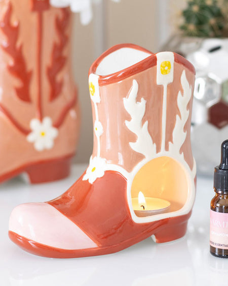 Close-up of a ceramic pink cowboy boot-shaped oil burner with floral details and an opening for a tealight candle