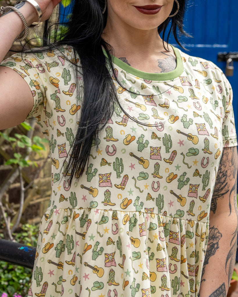 Close-up of the top half of a cream smock dress featuring colourful cowboy boots, cacti, stars, hats, guitars, and horseshoes on the fabric.