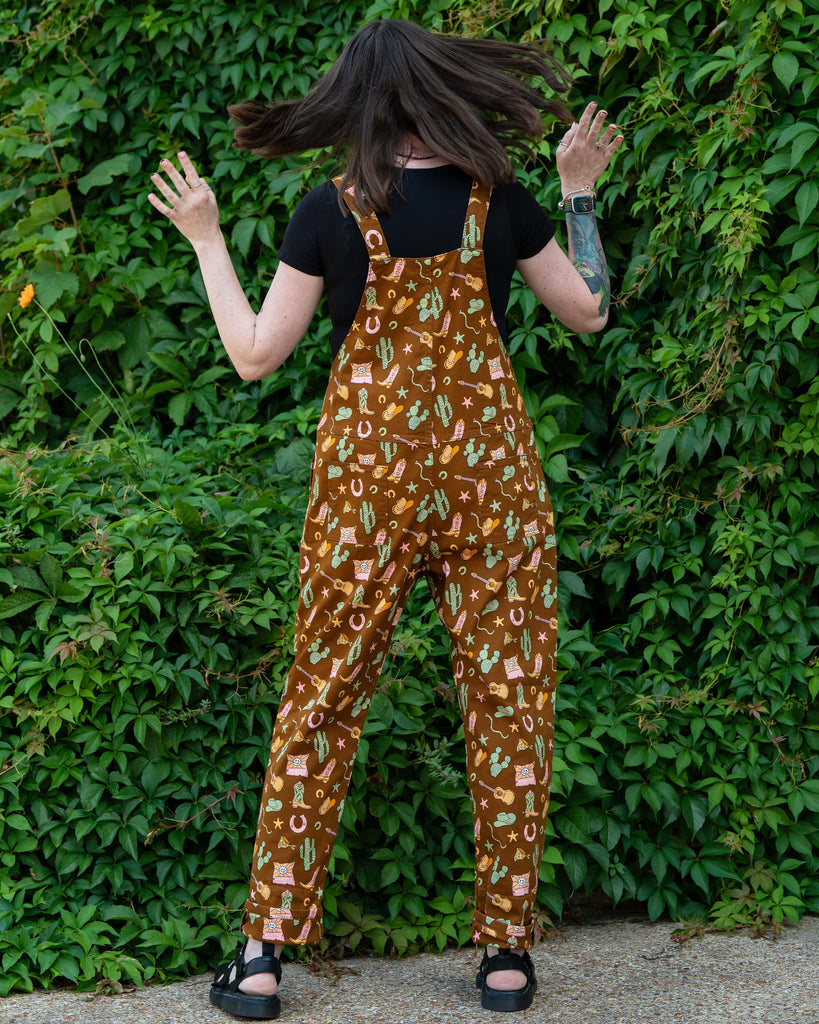 Back view of Rebel Romance x Yasmin Cousins Cowboy Dungarees, showing all-over western print with cacti, snakes, hats, boots and guitars.