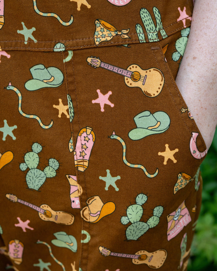 Close-up of the side pocket on Rebel Romance x Yasmin Cousins Cowboy Dungarees, printed with cowboy boots, guitars, cacti and stars.