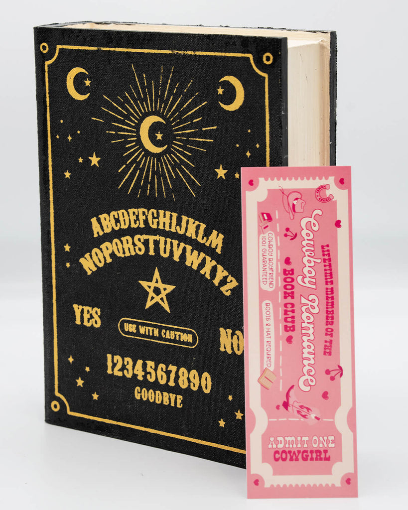 Cowboy Romance Book Club Bookmark from Rebel Romance displayed in a black and gold occult-themed book. Designed like a pink ticket, it features western-style typography and the phrase “Admit One Cowgirl.” A fun, flirty gift for cowboy romance readers and millennial book lovers with a love for bold and alternative stationery.