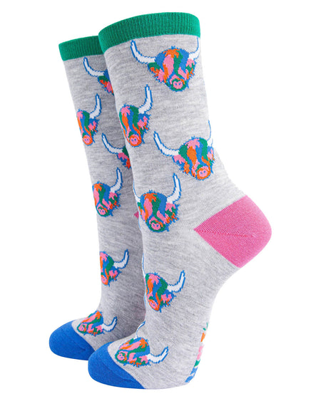  (Socks Standing Up): A pair of grey bamboo socks with rainbow Highland cow print displayed upright. The bold multicoloured design is complemented by a green cuff, pink heel, and blue toe.