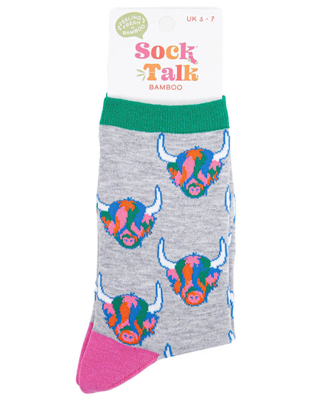 (Packaged Socks): A folded pair of rainbow Highland cow socks inside their Sock Talk bamboo packaging, featuring the quirky, colourful cow design on a light grey base. The packaging states a UK 3-7 size range.