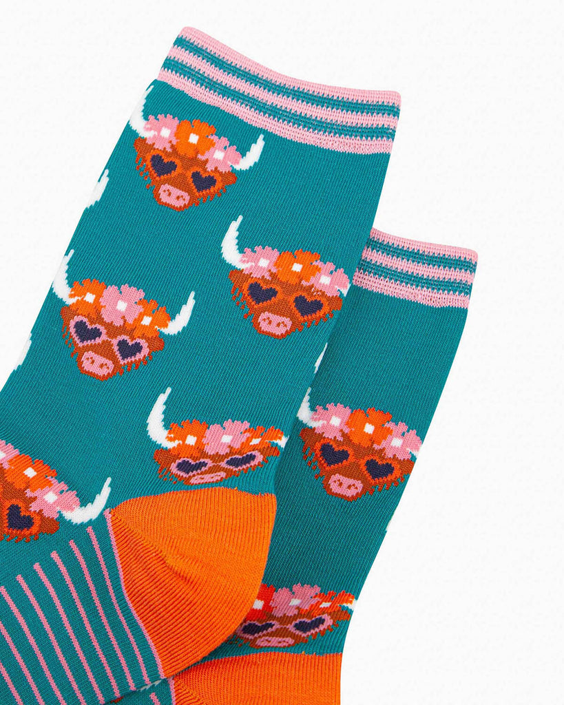 (Close-Up of Design): A detailed close-up of the bamboo socks, showing the Highland cow’s fuzzy face, flower crown, and heart-shaped sunglasses, along with the striped cuff for extra detail.